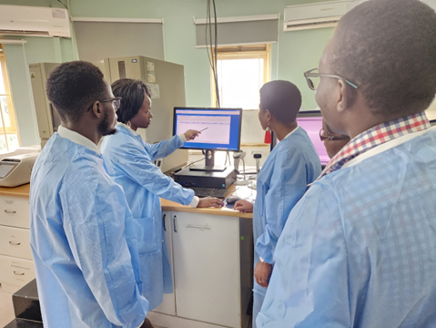 Image of Core C Uganda staff gathered around a computer screen in their lab
